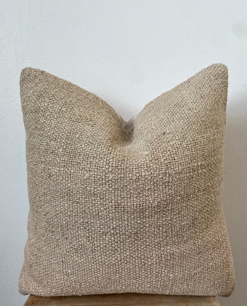 Textured beige pillow on a wooden stool against a white background