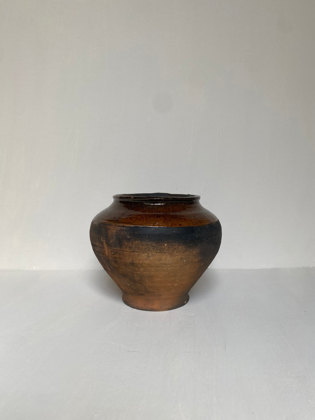 A small brown antique clay pot on a cream background
