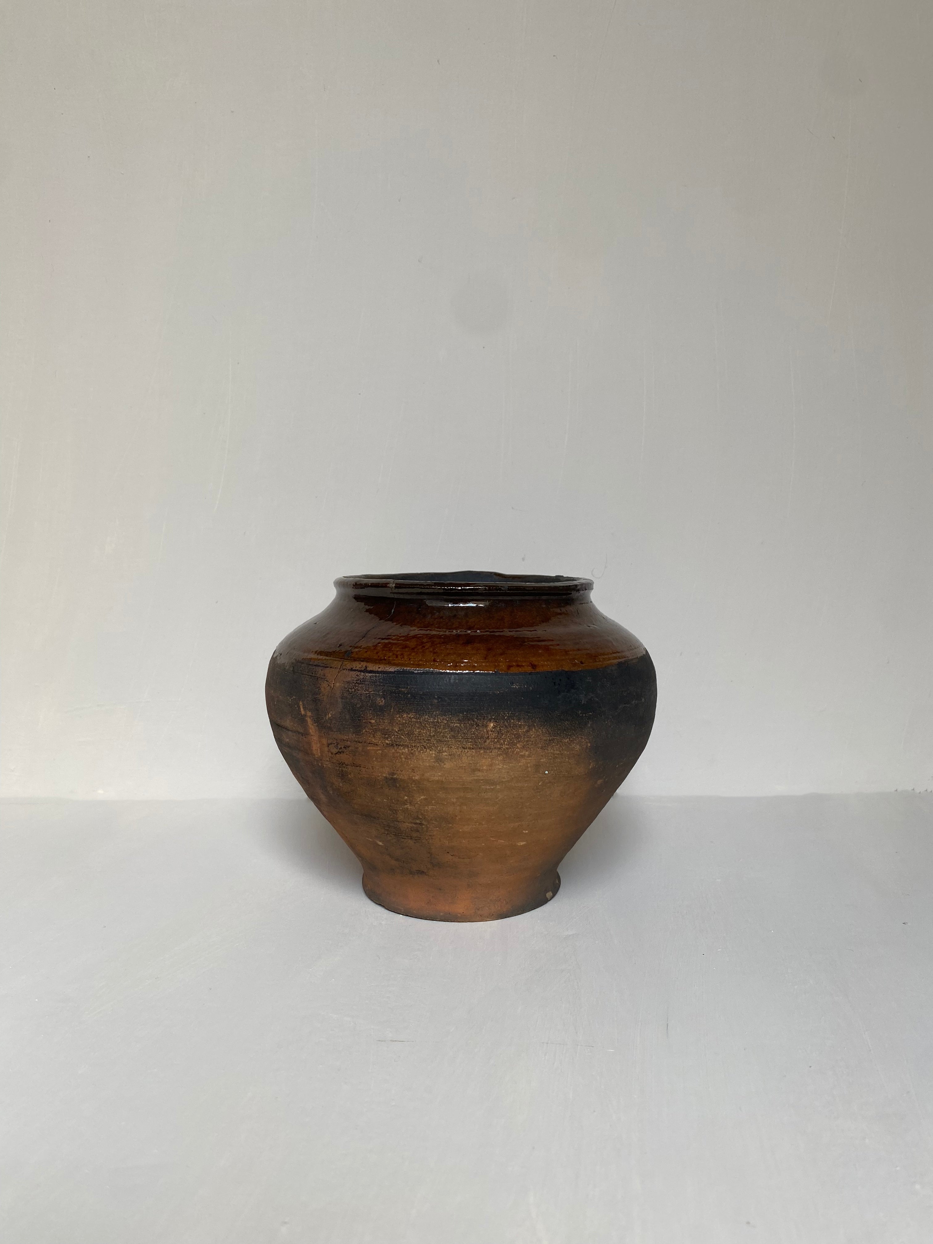 A small brown antique clay pot on a cream background