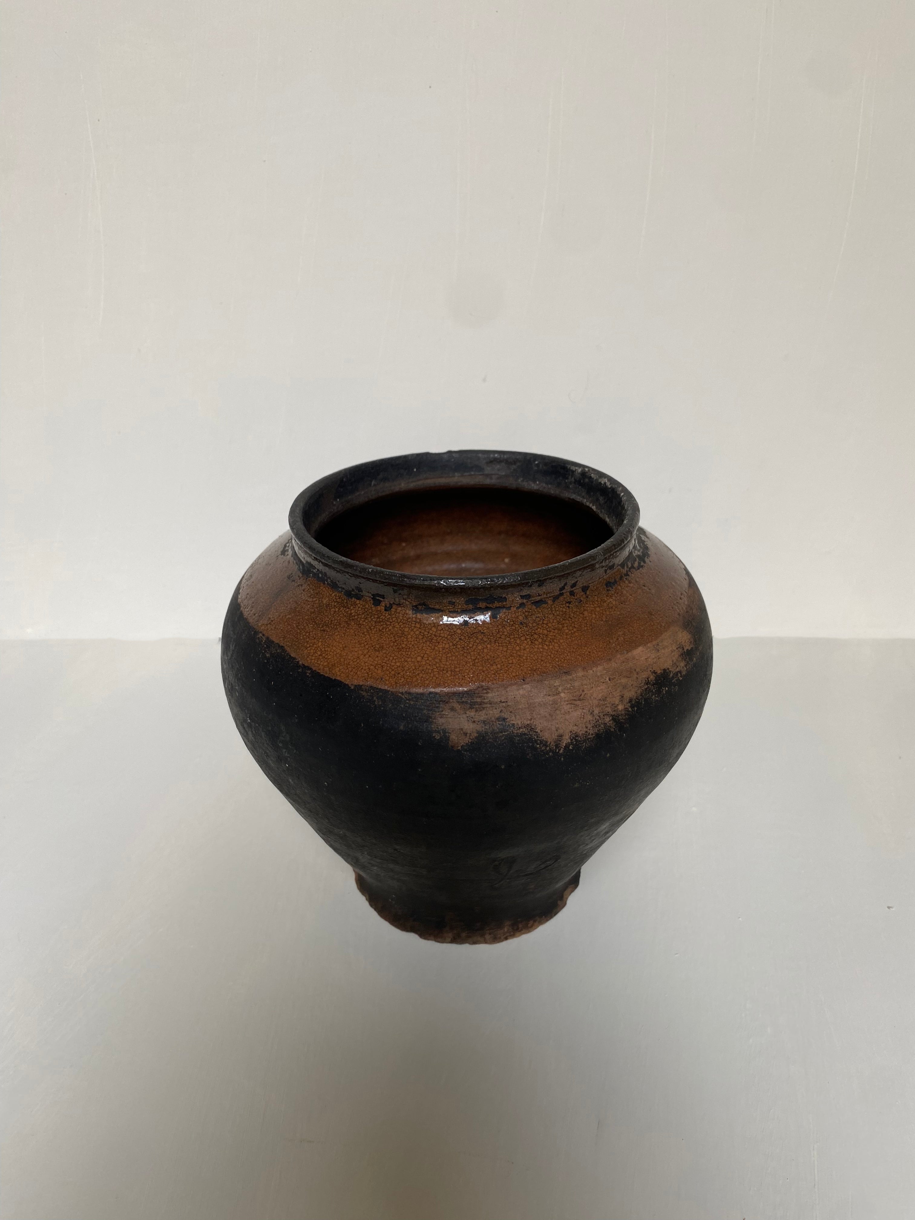 Black and brown antique terracotta clay pot on a cream background