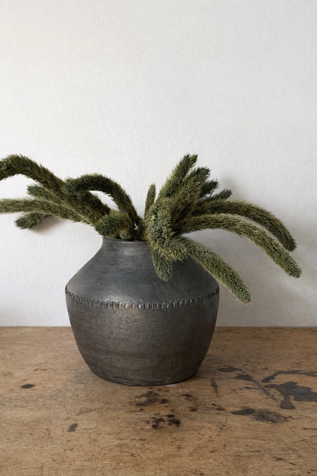 Small antique style clay pot with green flowers inside on a table with books 