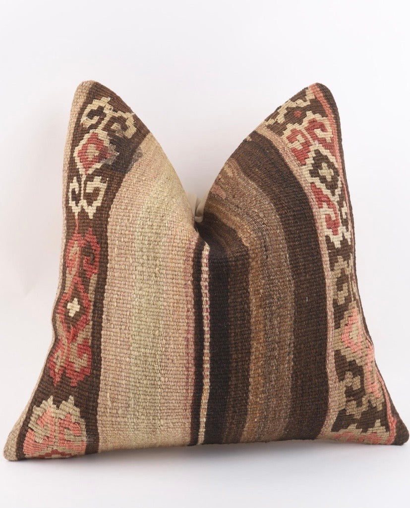 A square Turkish Kilim pillow cover featuring a traditional kilim pattern in shades of brown, beige, and muted red, set against a plain white background.