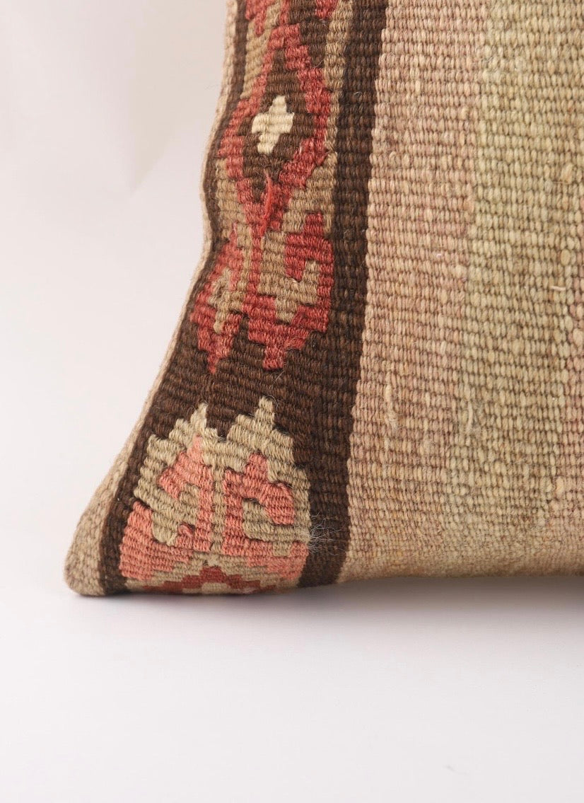 Close-up of a Anatolian Turkish pillow cover showing a textured beige body with a dark brown border and red, pink, and cream geometric pattern.