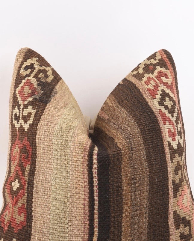 A close-up of a Turkish Kilim pillow cover woven throw pillo showing its textured kilim pattern with stripes of brown, beige, and red on a cream backend