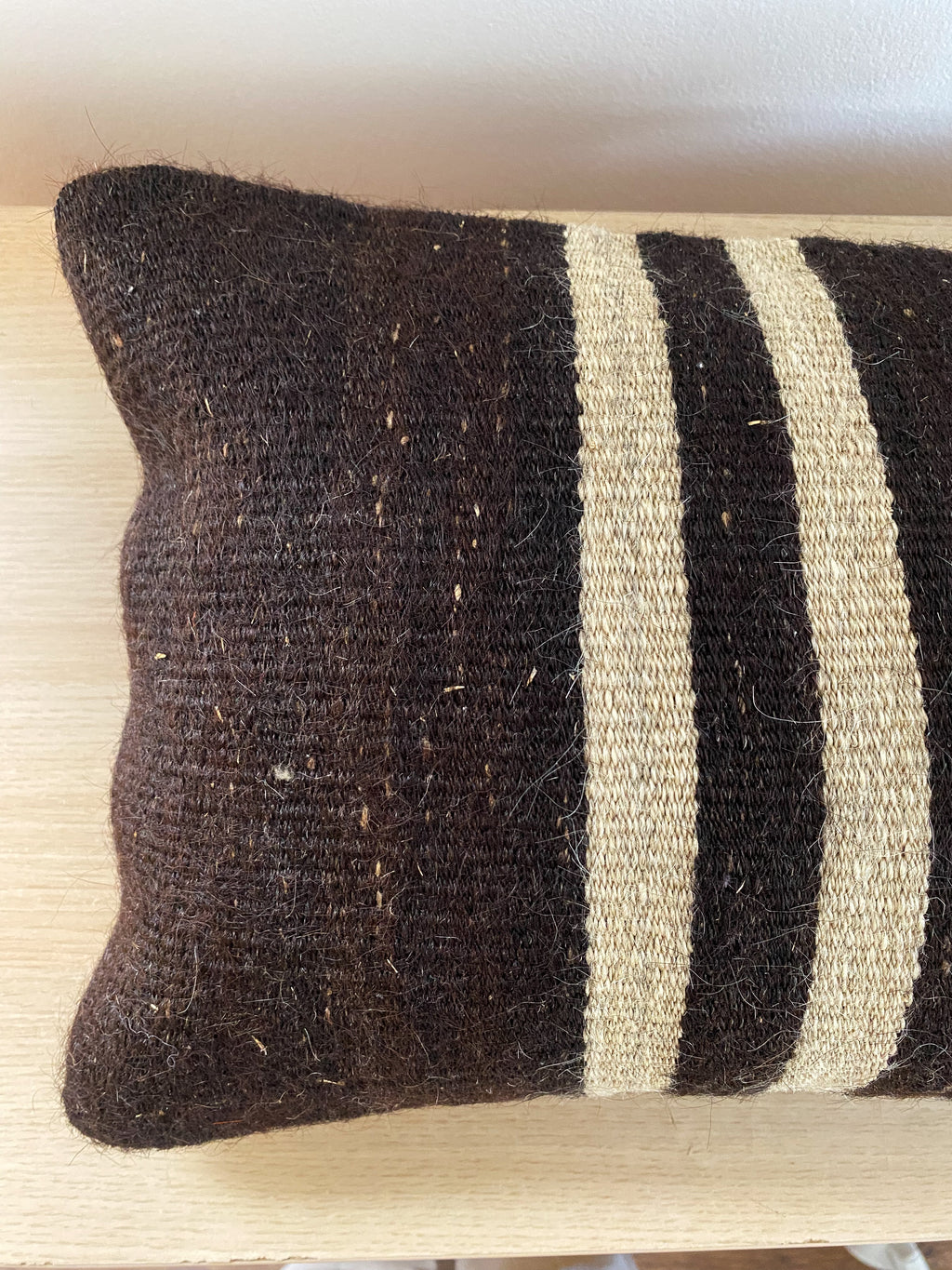 Textured Turkish Kilim pillow cover with dark brown, black and beige stripes on a wooden surface