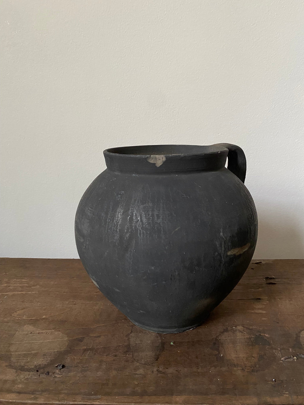 Black vintage clay pot on a wooden surface with a white background