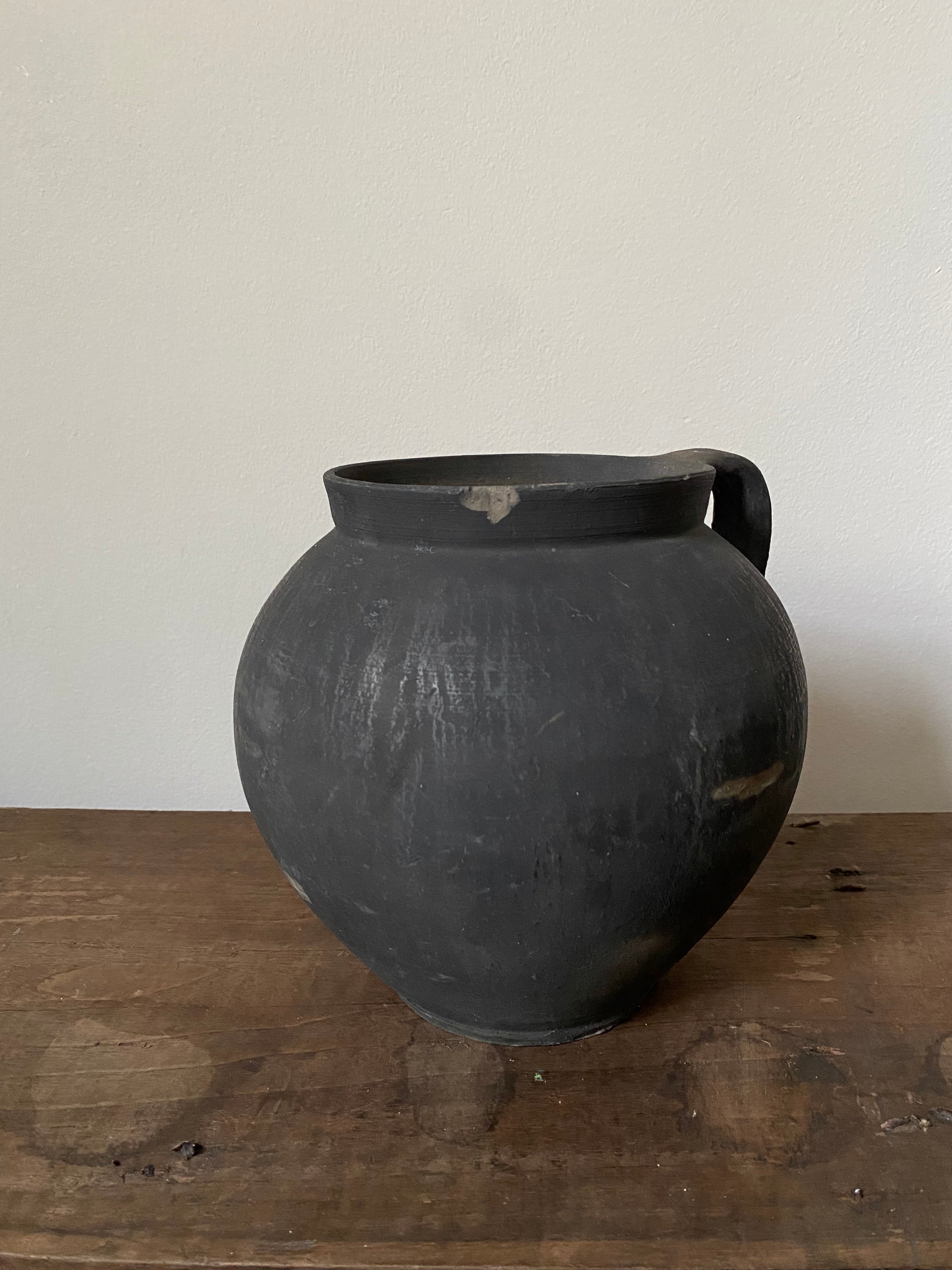 Black vintage clay pot on a wooden surface with a white background