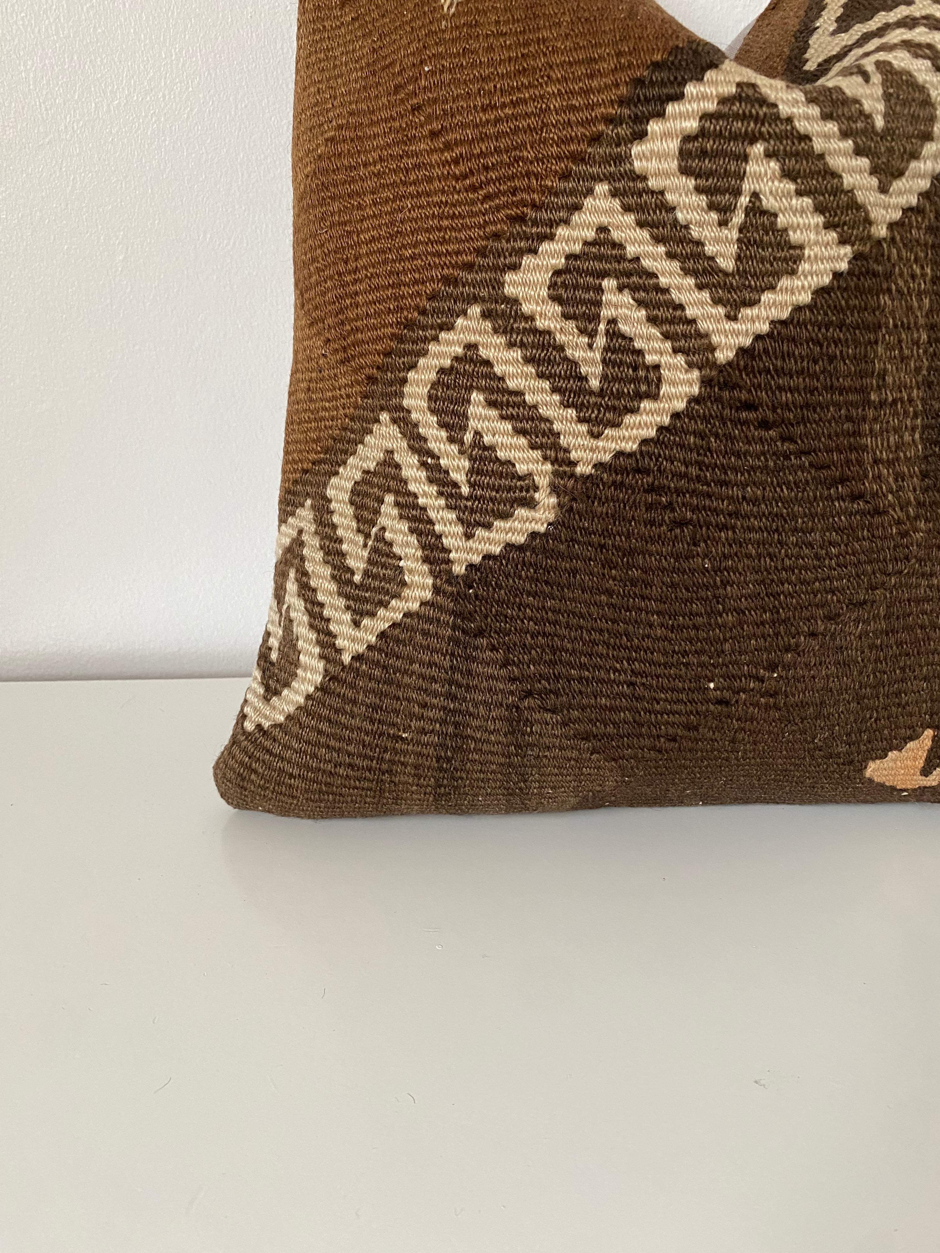 Brown Turkish kilim pillow cover with geometric pattern on a white surface