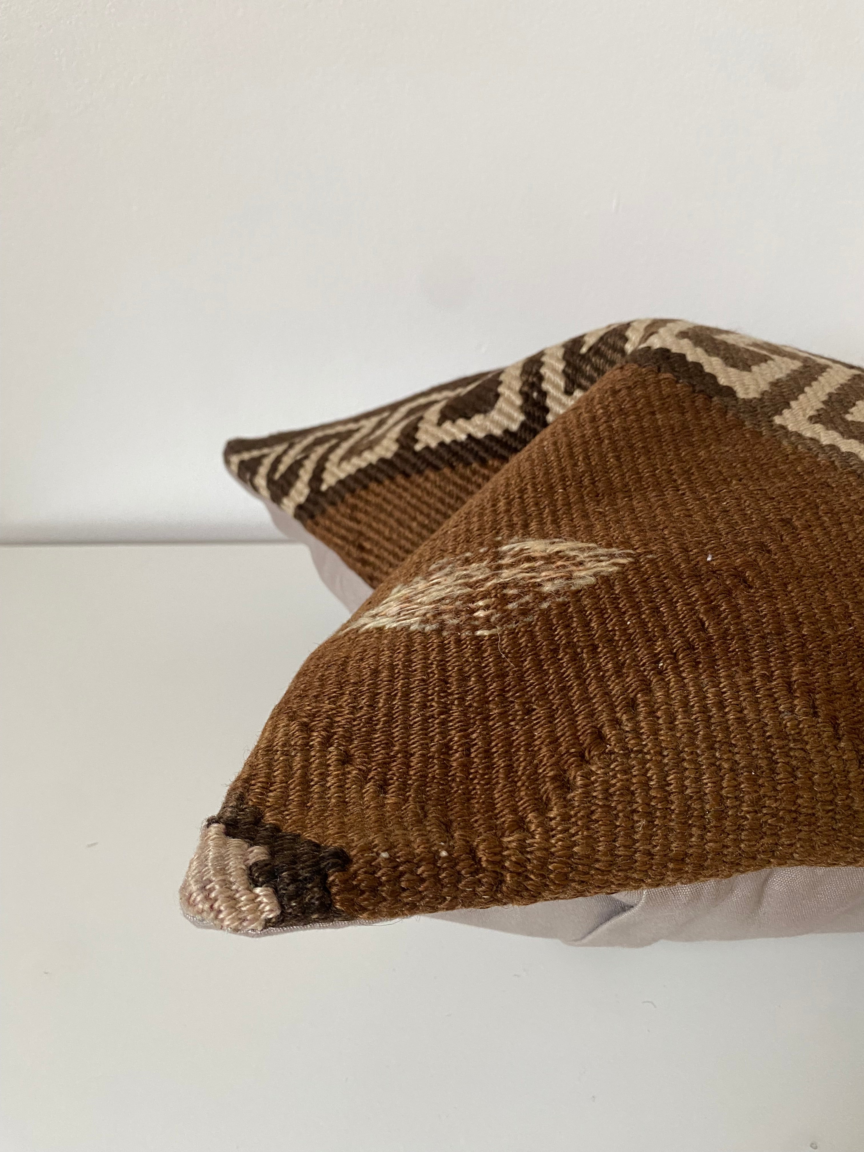 Brown wool Turkish kilim pillow cover with geometric pattern draped over a white surface