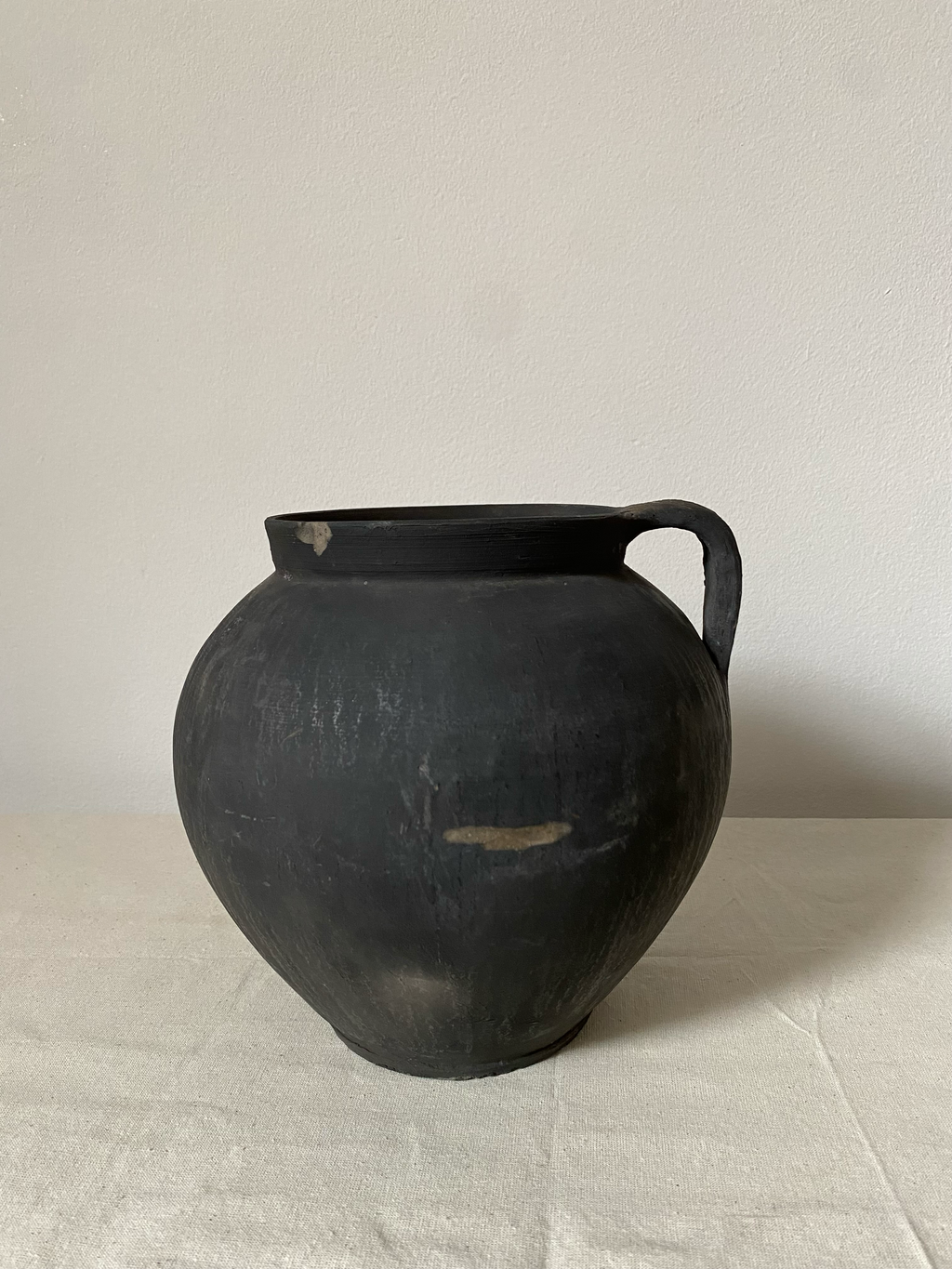 Black ceramic pitcher on a light grey surface with a neutral background