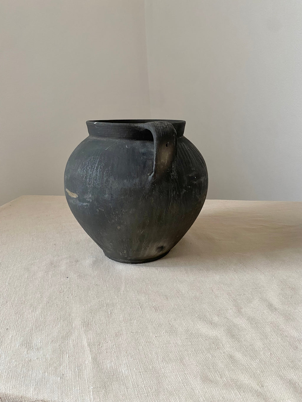 Black antique clay pot on a light gray surface with a neutral background