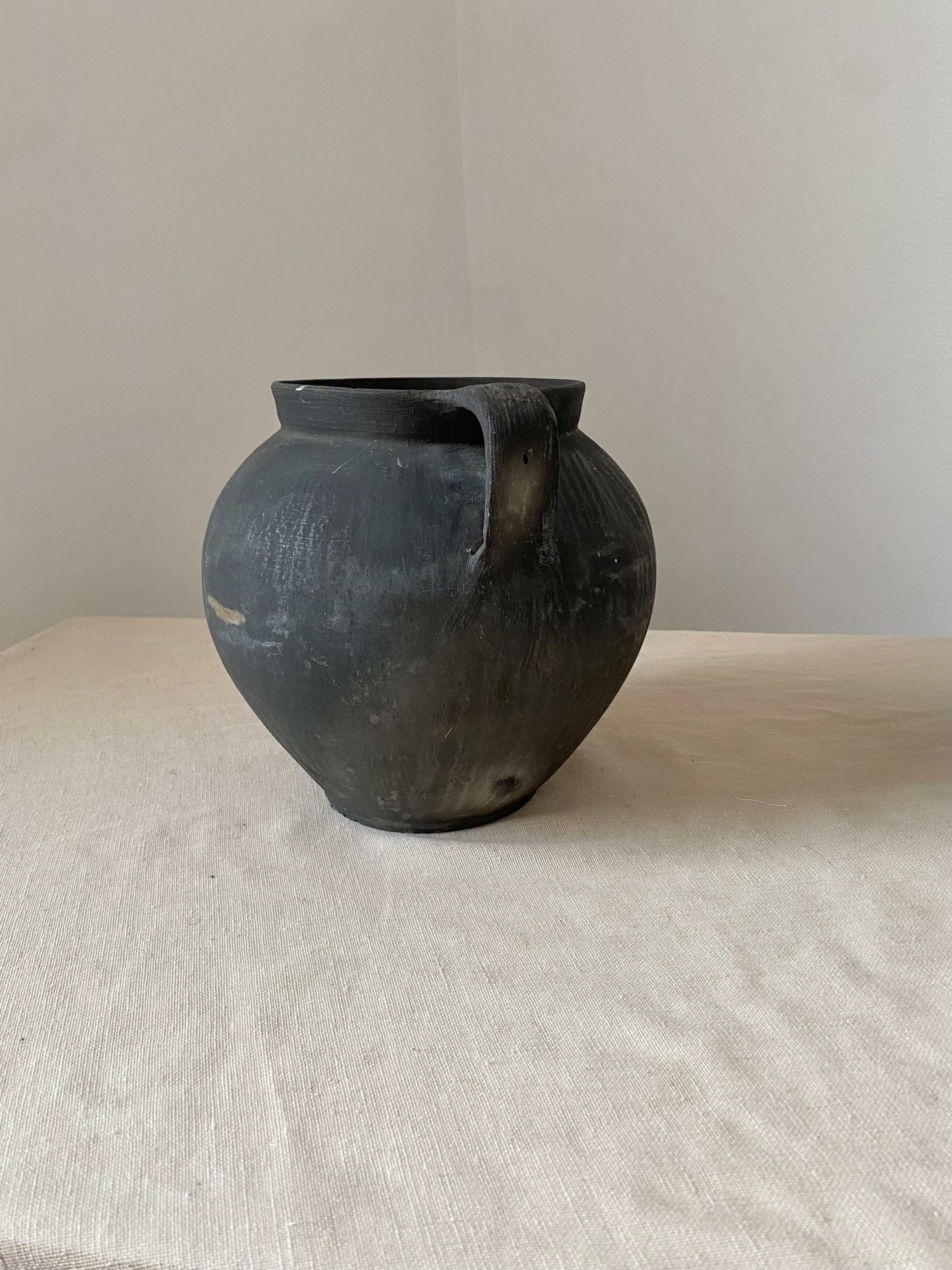 Black antique clay pot on a light gray surface with a neutral background