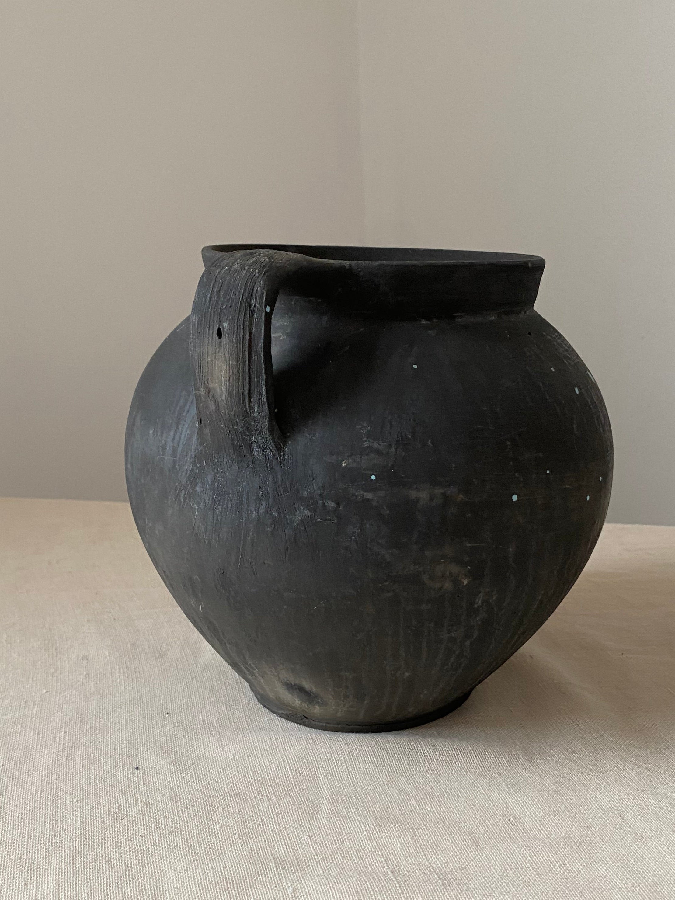 Black antique clay pot on a textured white surface