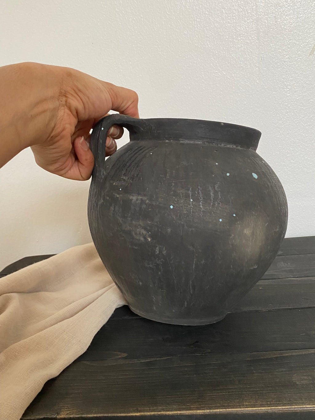 Black antique clay pot on a wooden bench leaning against a wall