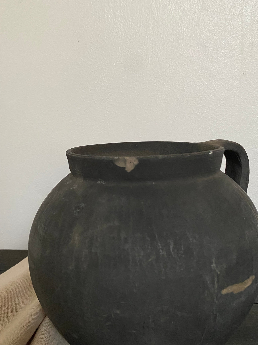 Black antique clay pot on a wooden bench against a light neutral background