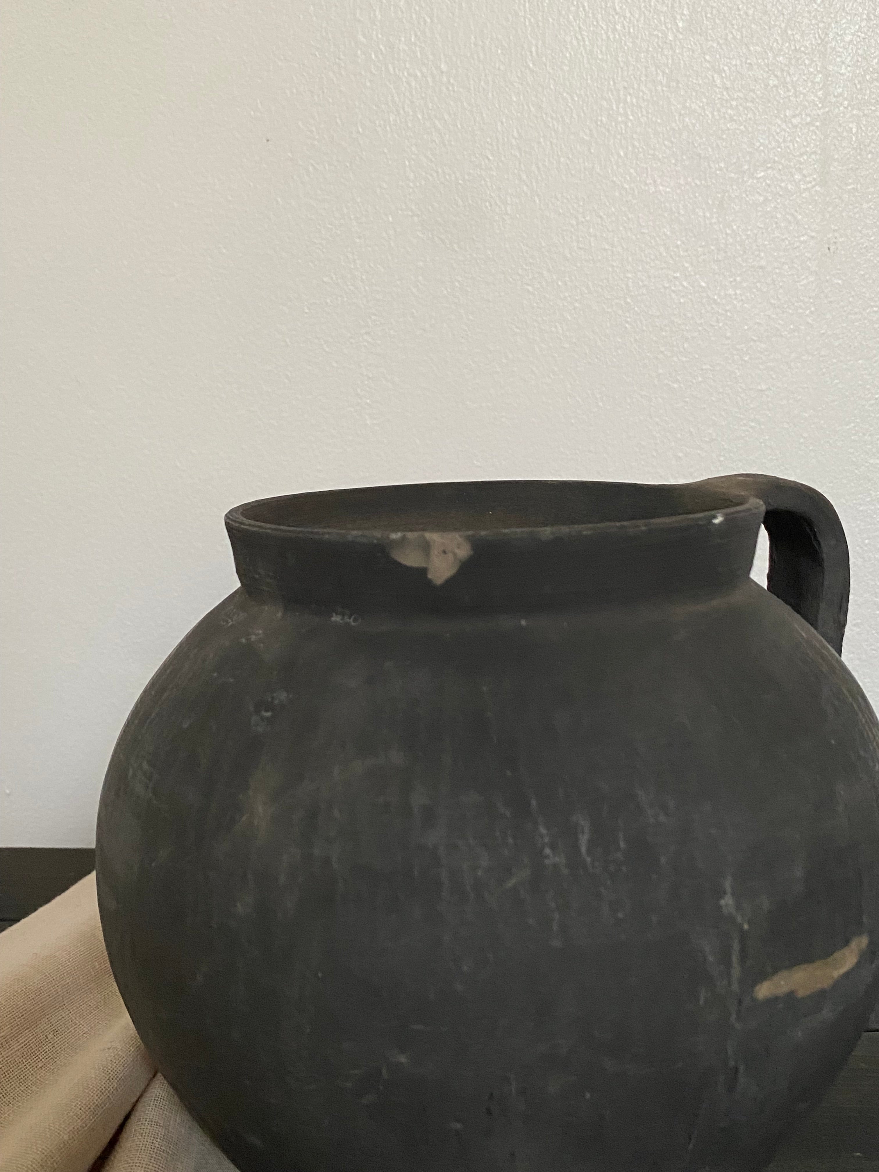 Black antique clay pot on a wooden bench against a light neutral background