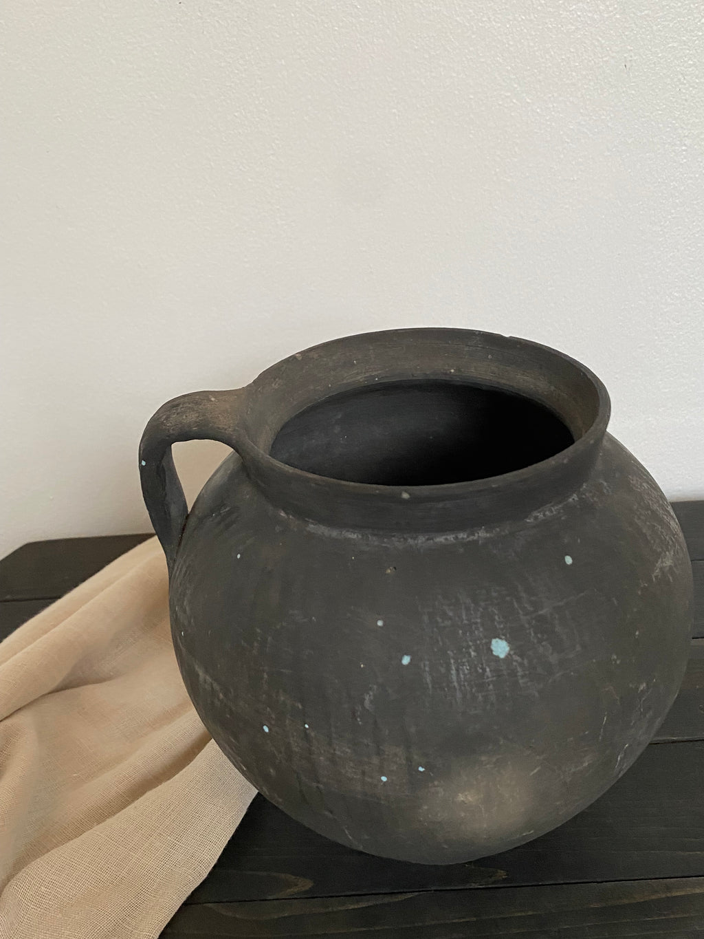 Black antique clay pot on a wooden bench leaning against a wall