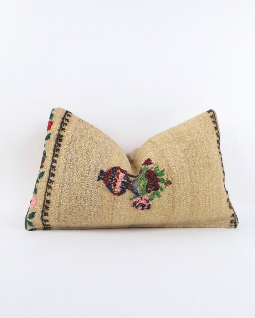 A rectangular Turkish Kilim beige cushion cover woven throw pillow with a central embroidered motif of a bird holding a green wreath, bordered by black geometric patterns on the sides, set against a plain white background.