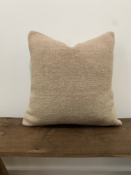 Textured beige Kilim pillow cover on a wooden surface with a neutral background