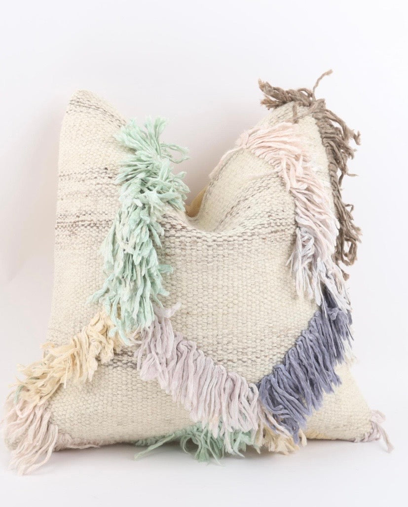 A square woven Turkish Kilim pillow cover in a natural beige tone with colourful fringe accents in mint green, dusty blue, cream, and taupe, set against a plain white background.