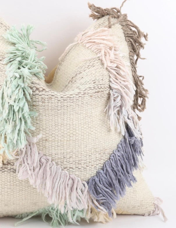 A close-up of a Turkish Kilim pillow cover with a warm cream colour, decorated with soft pastel fringe tassels in mint green, pale pink, and light