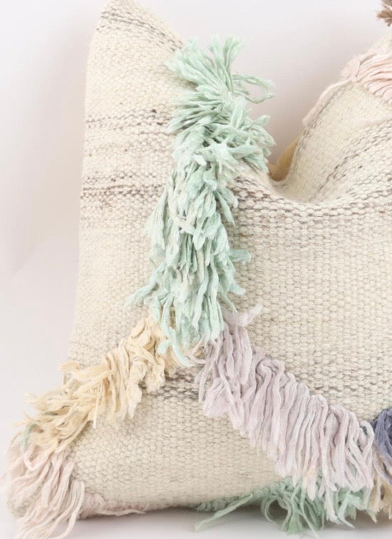 A close-up of a Turkish Kilim pillow cover with a warm cream colour, decorated with soft pastel fringe tassels in mint green, pale pink, and light