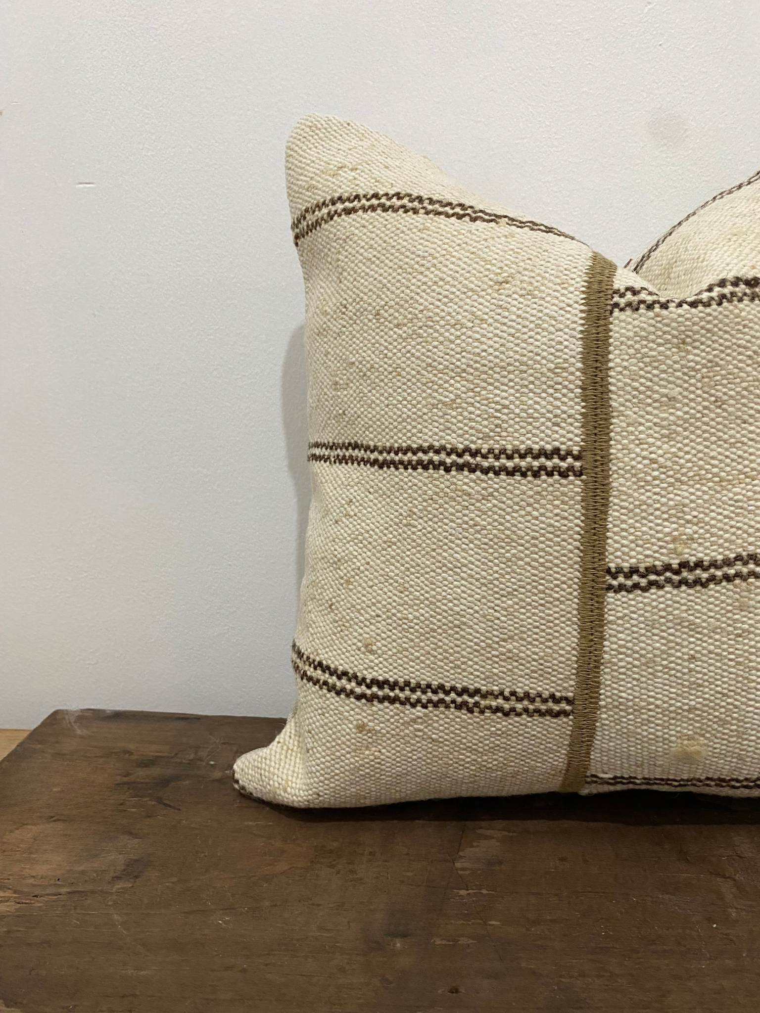 Textured Turkish Kilim pillow cover with brown stripes on a wooden surface against a white wall