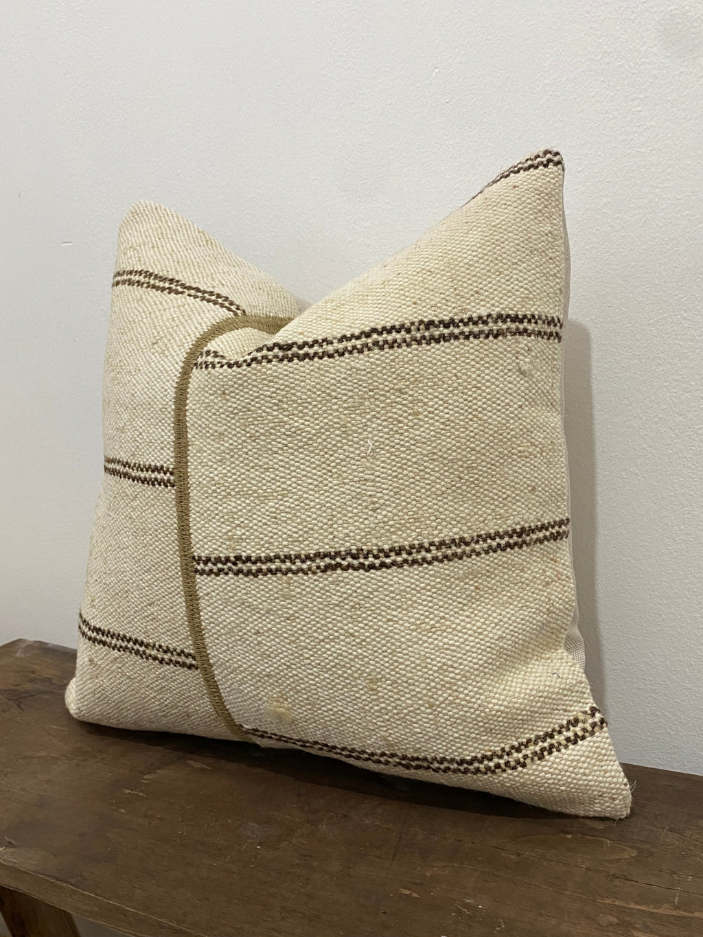 Textured Turkish Kilim pillow cover with brown stripes on a wooden surface against a white wall