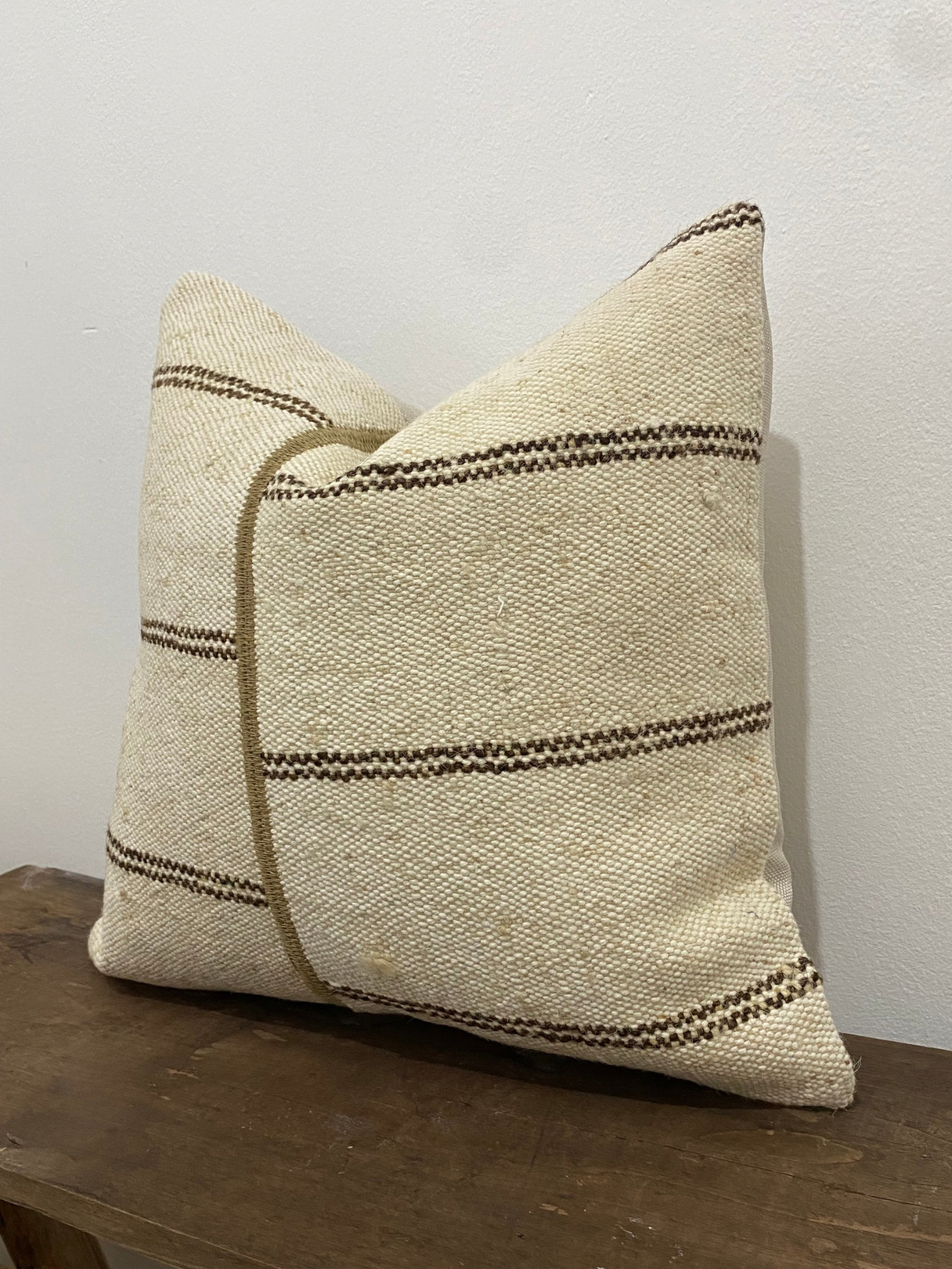 Textured Turkish Kilim pillow cover with brown stripes on a wooden surface against a white wall