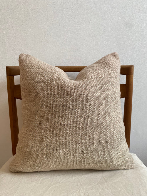 Textured beige Turkish Kilim pillow cover on a wooden headboard against a light gray wall.