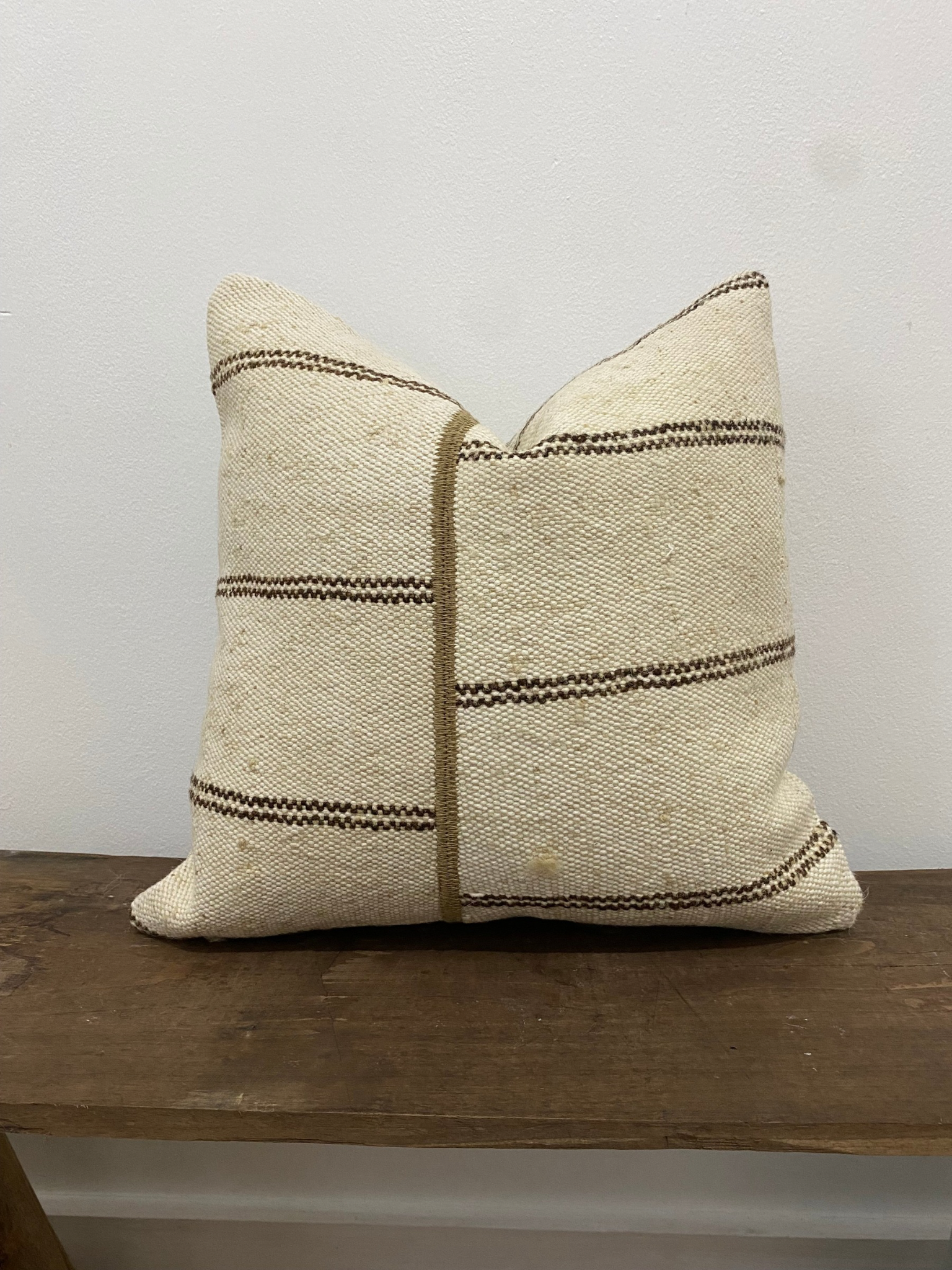 Textured Turkish Kilim pillow cover with striped pattern on a wooden surface against a white background