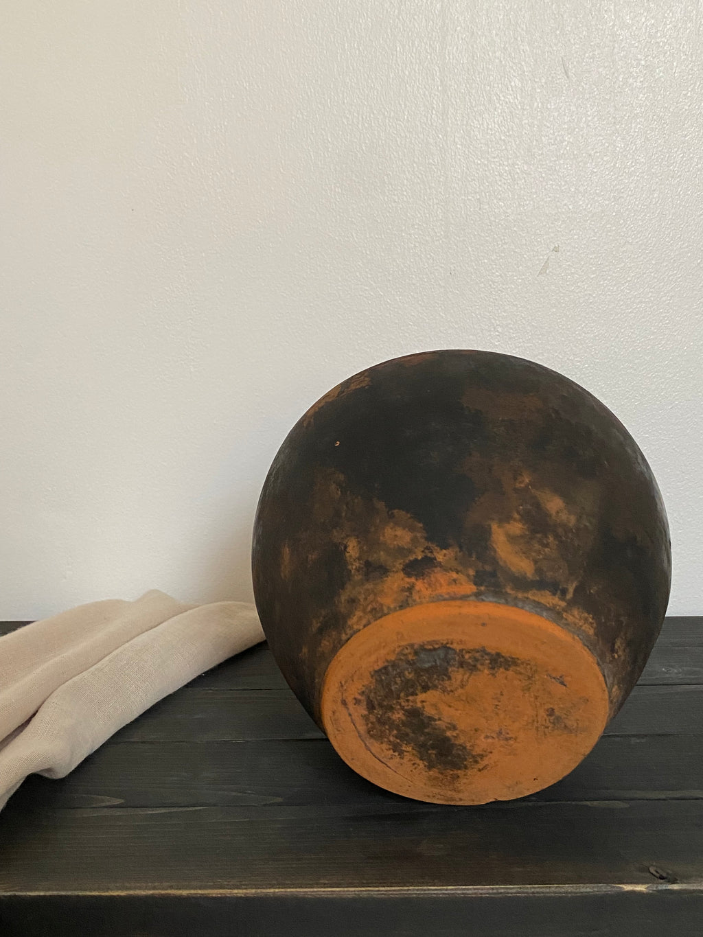 Back of an antique terracotta clay pot on a white wall with a dark wooden surface