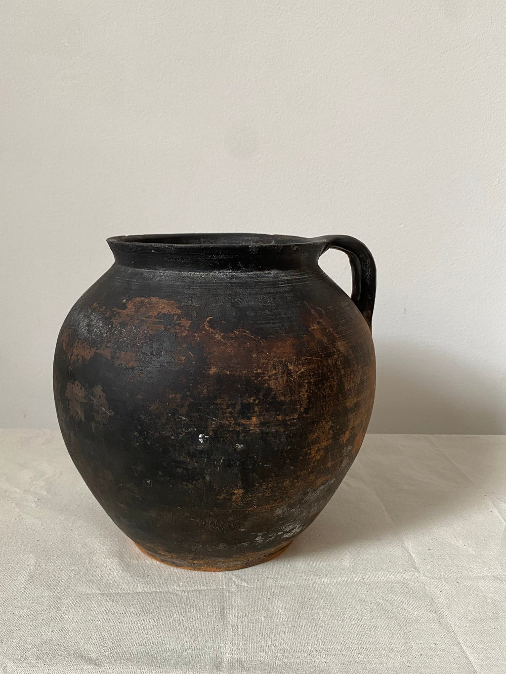 Black antique clay pot with a textured surface on a light grey background