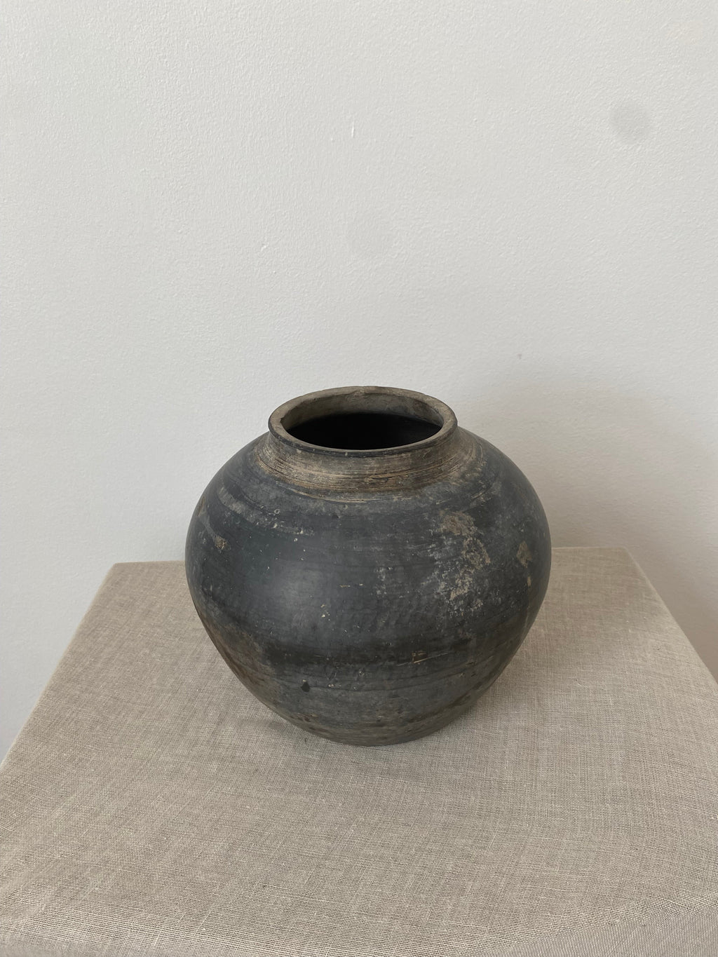 Dark grey antique clay pot on a textured beige linen fabric with a white background