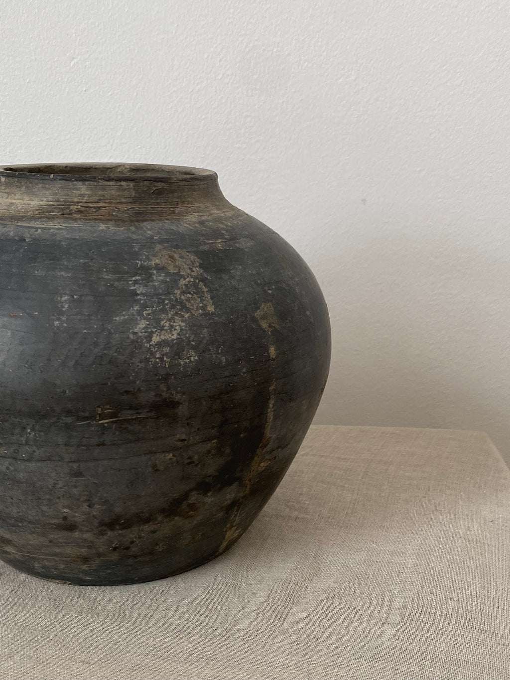 Dark grey antique clay vessel on light beige linen fabric