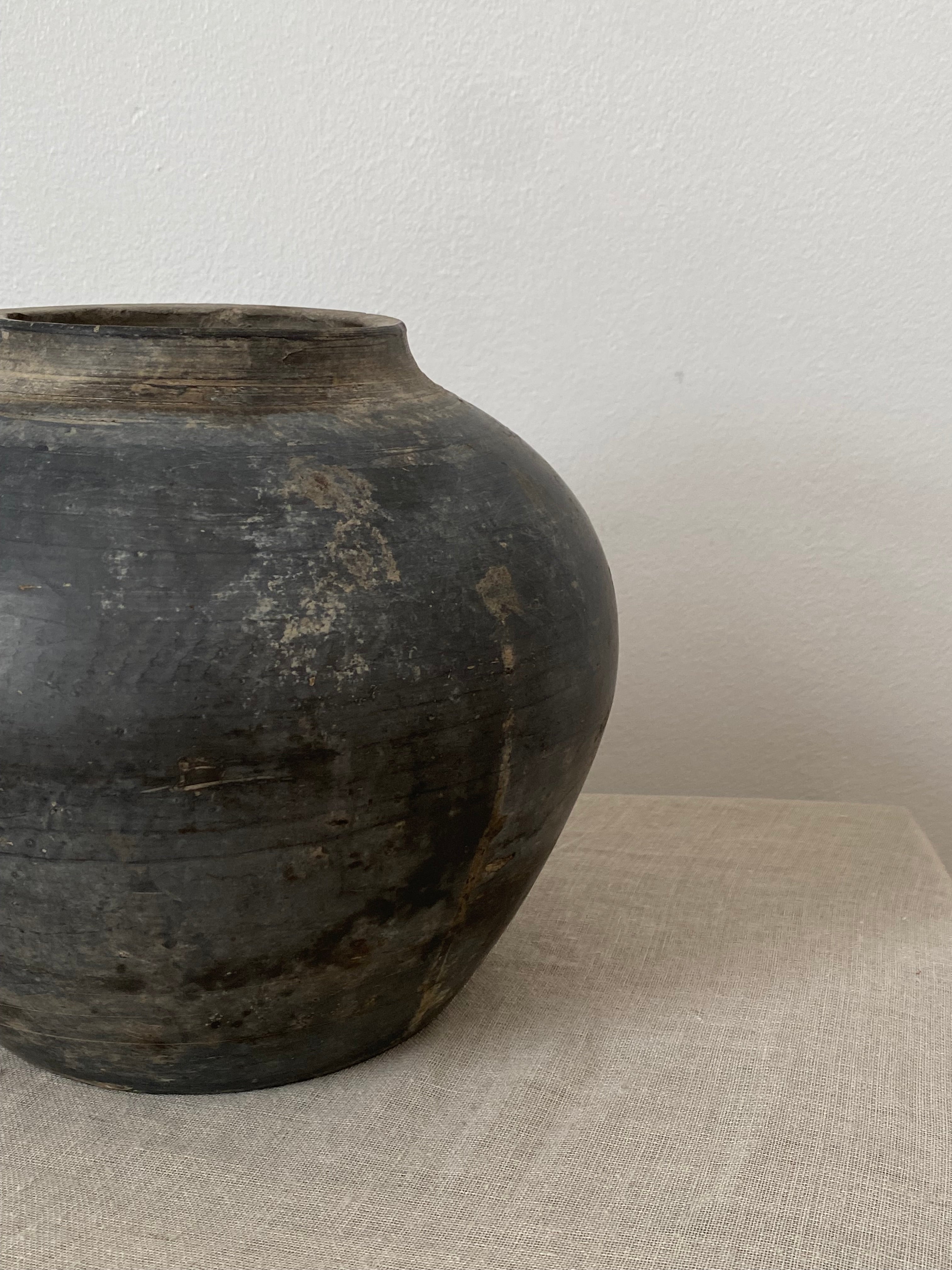 Dark grey antique clay vessel on light beige linen fabric