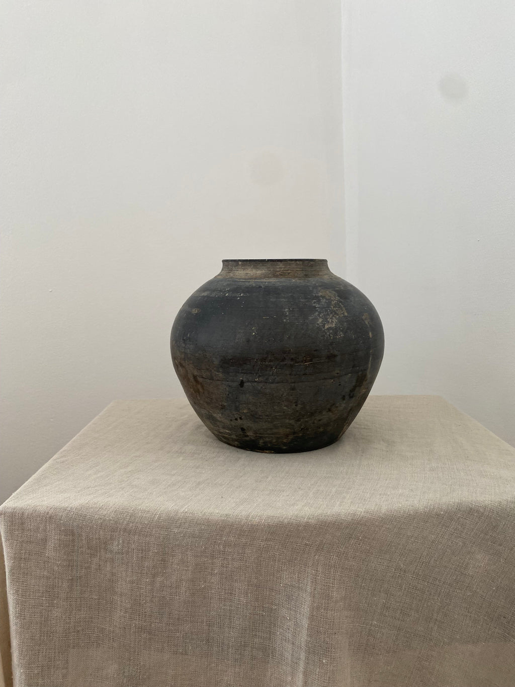 Black clay vessel on a white surface with a gray textured surface in the background