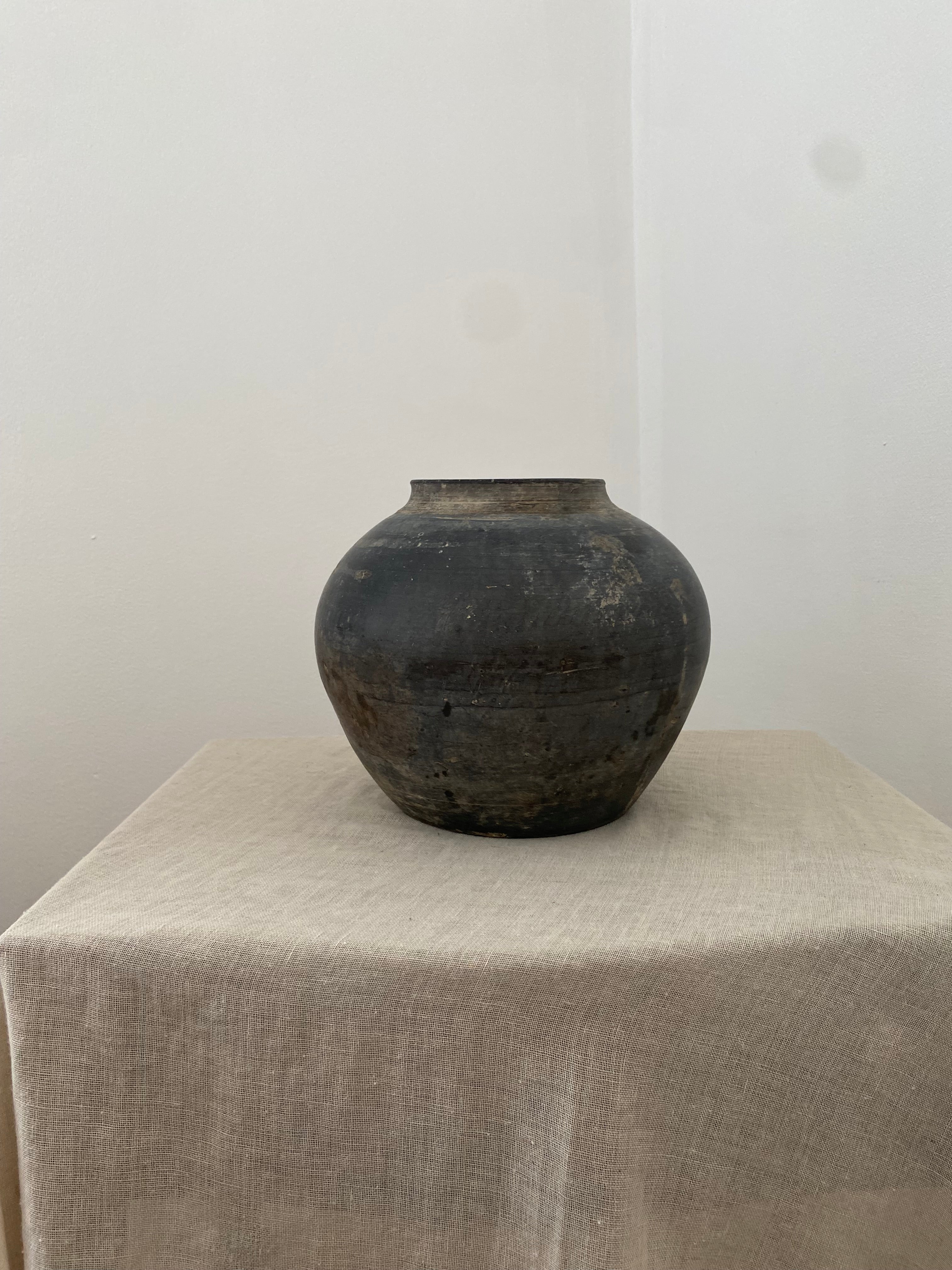 Black clay vessel on a white surface with a gray textured surface in the background