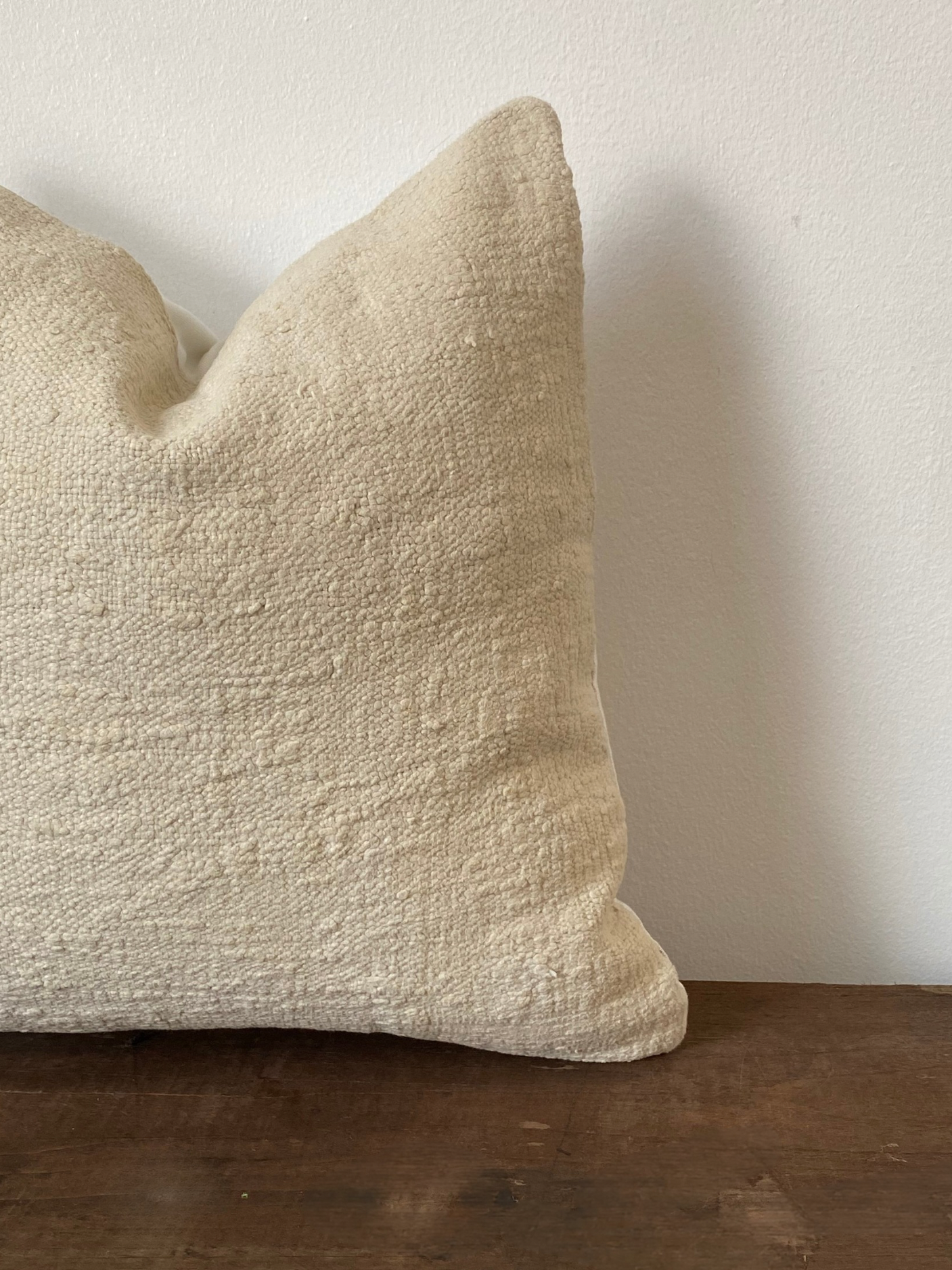 Textured off white pillow cover on a wooden surface with a plain background