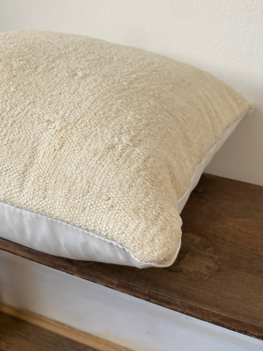 Textured off white pillow cover on a wooden shelf against a white wall