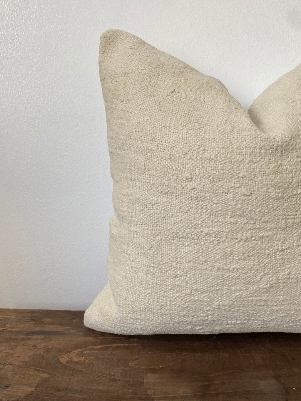 Textured off white pillow cover on a wooden surface with a white background