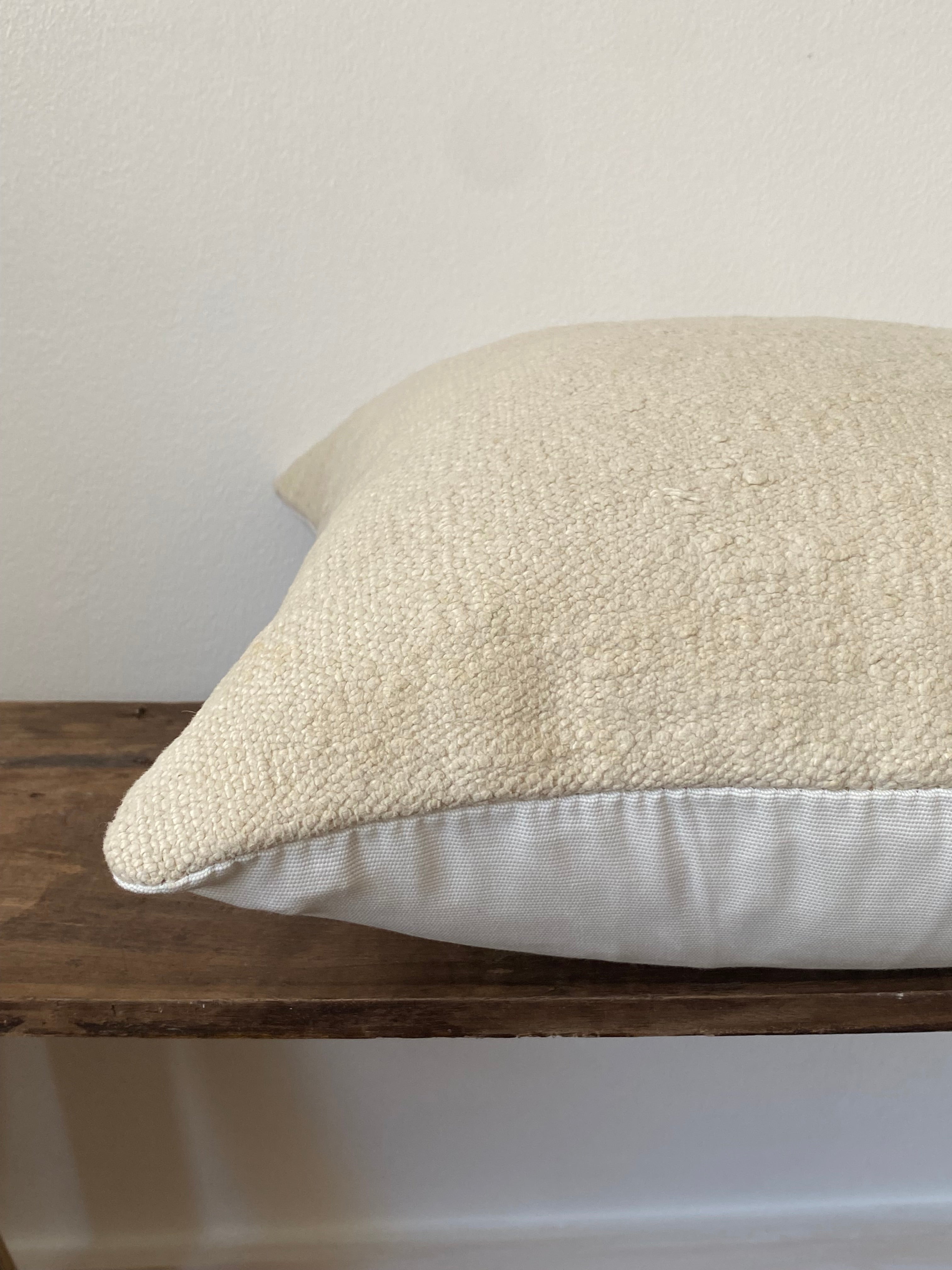 Textured off white pillow cover on a wooden stand against a white wall