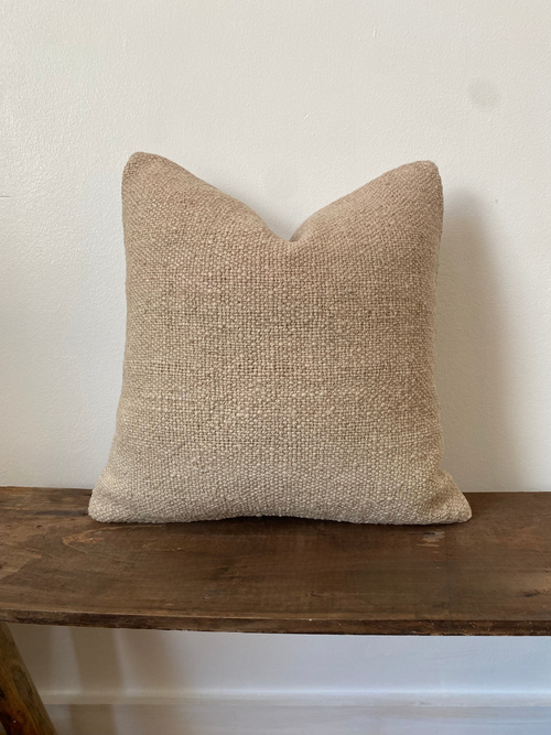 Beige textured Turkish Kilim pillow cover on a wooden surface with a white wall background