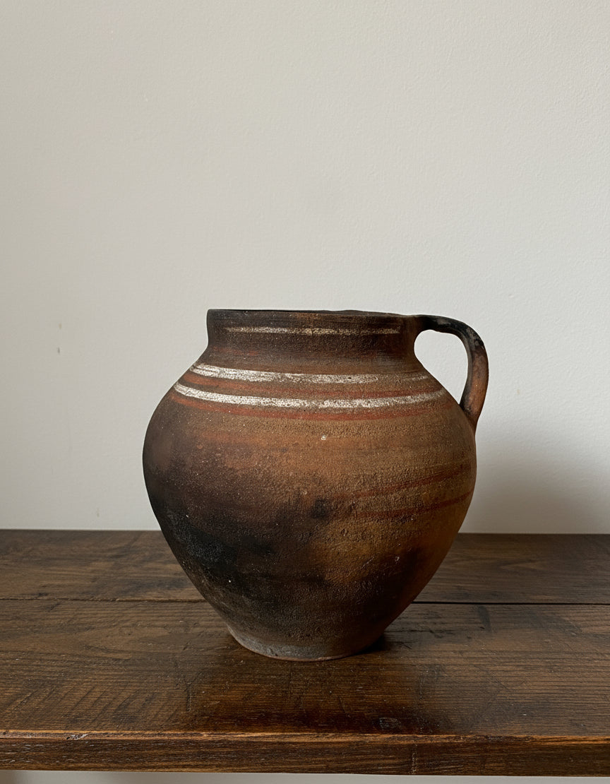 Brown earthenware vase with a handle on a light gray background