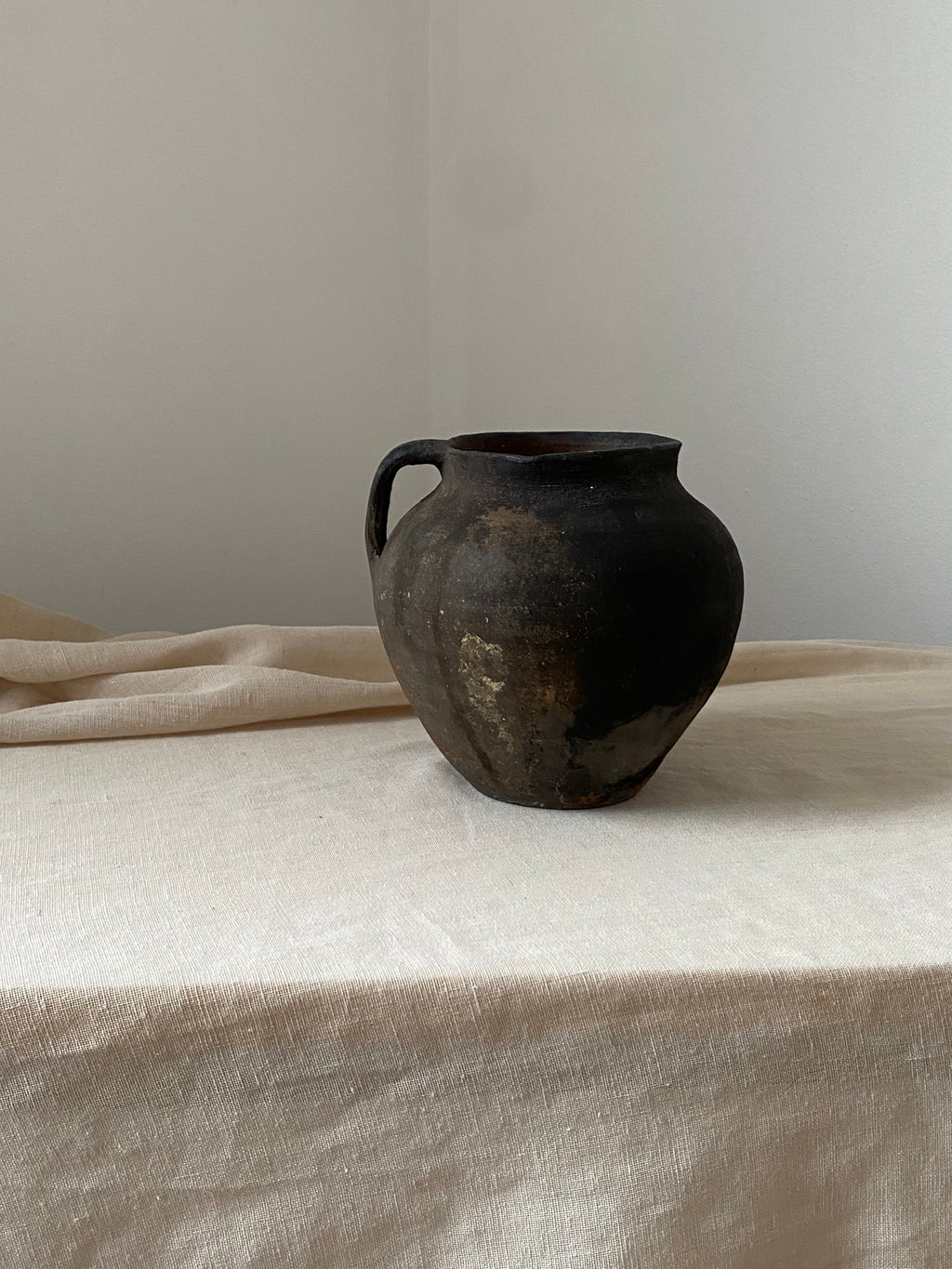 Black antique clay pot leaning against a light-colored curtain on a neutral background