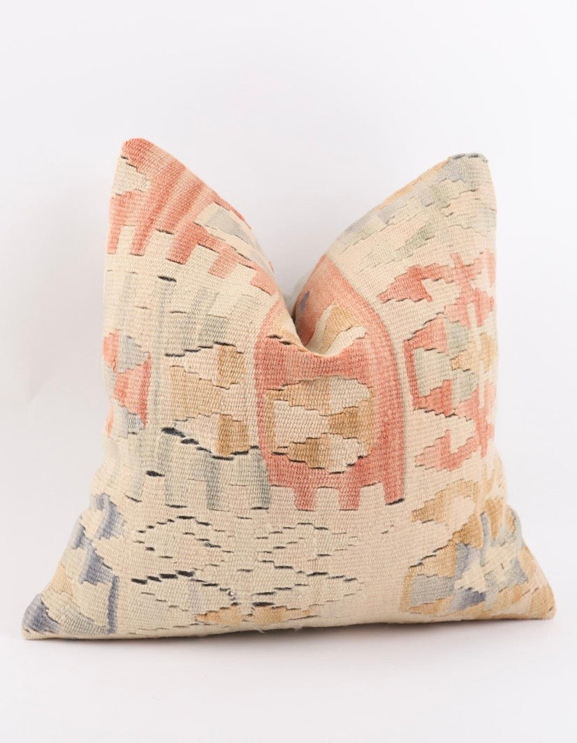 A square decorative Turkish Kilim pillow cover with a woven kilim-style geometric pattern in beige, terracotta, and muted blue-gray, photographed against a clean white background.